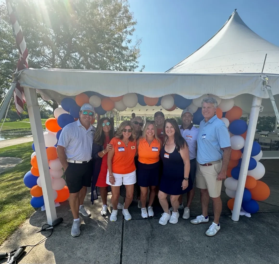 Group gathered under tent with orange, blue, and white balloons