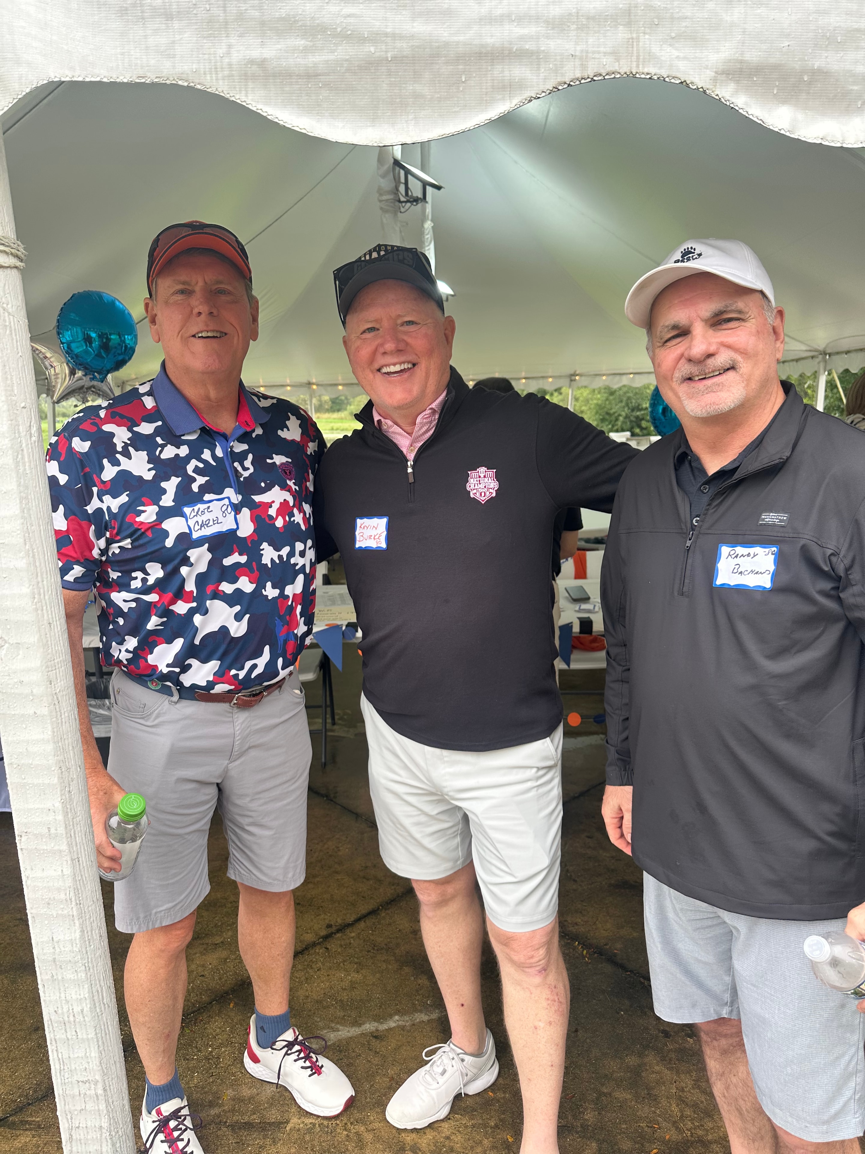 Three men posing at golf event tent