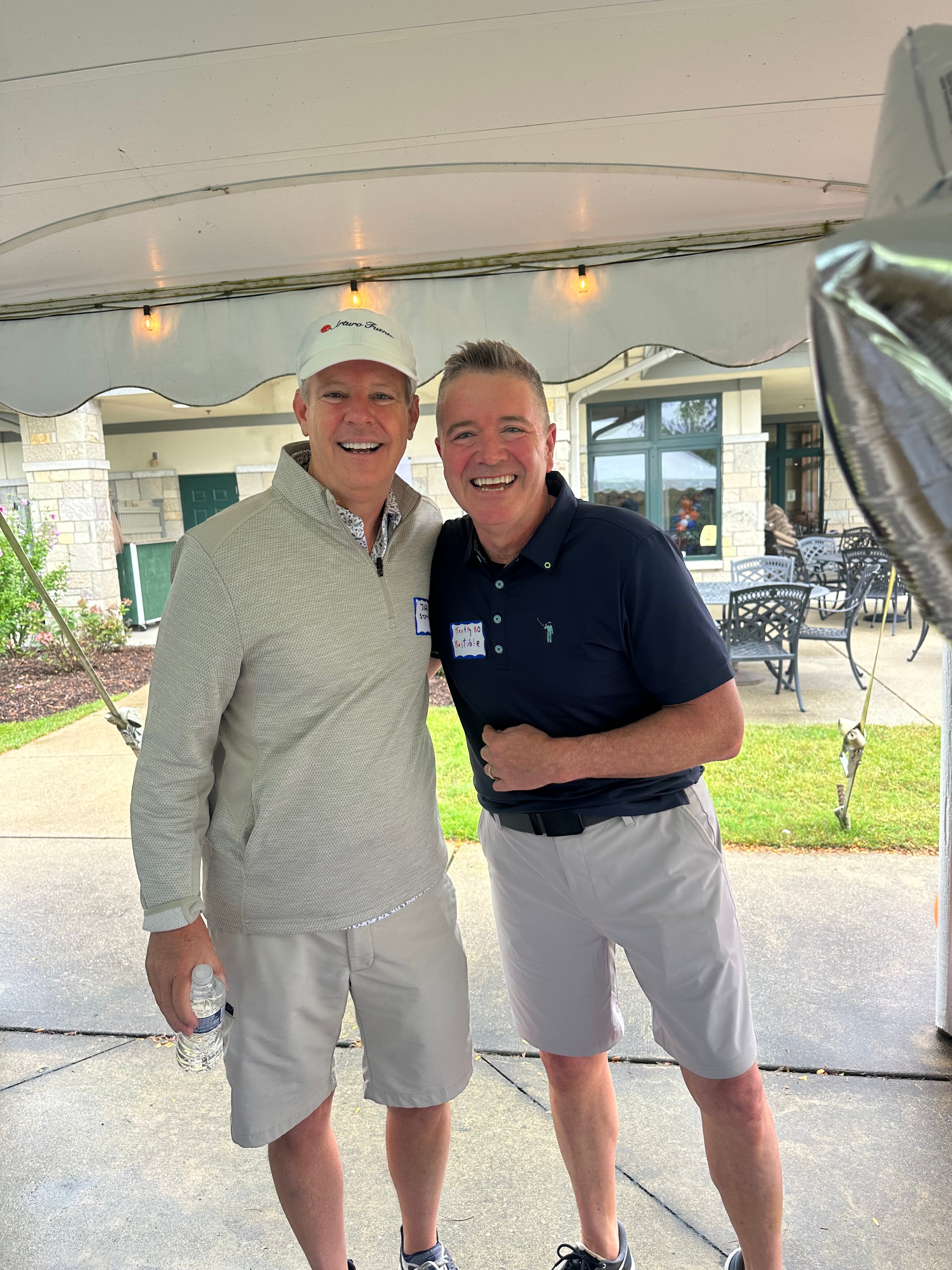 Two men posing at golf event tent