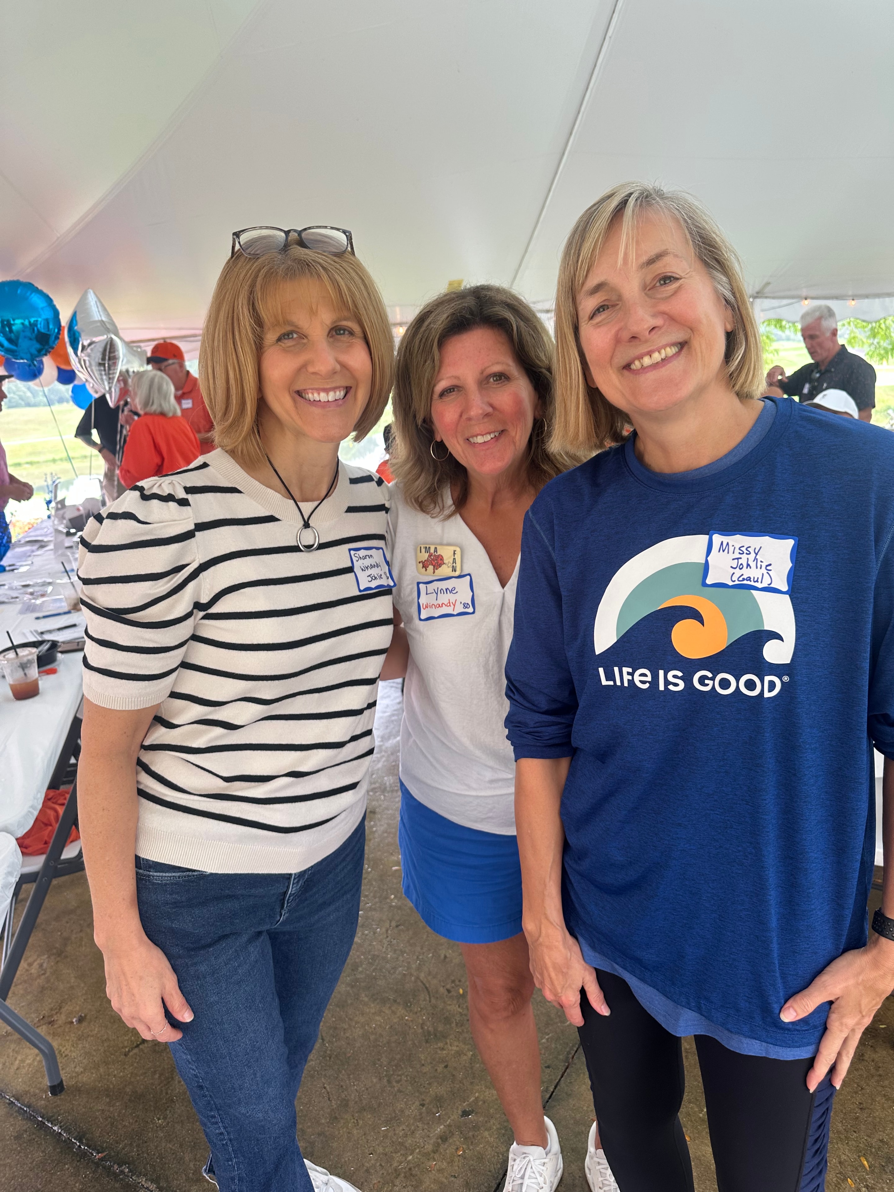 Three women smiling at outdoor event tent