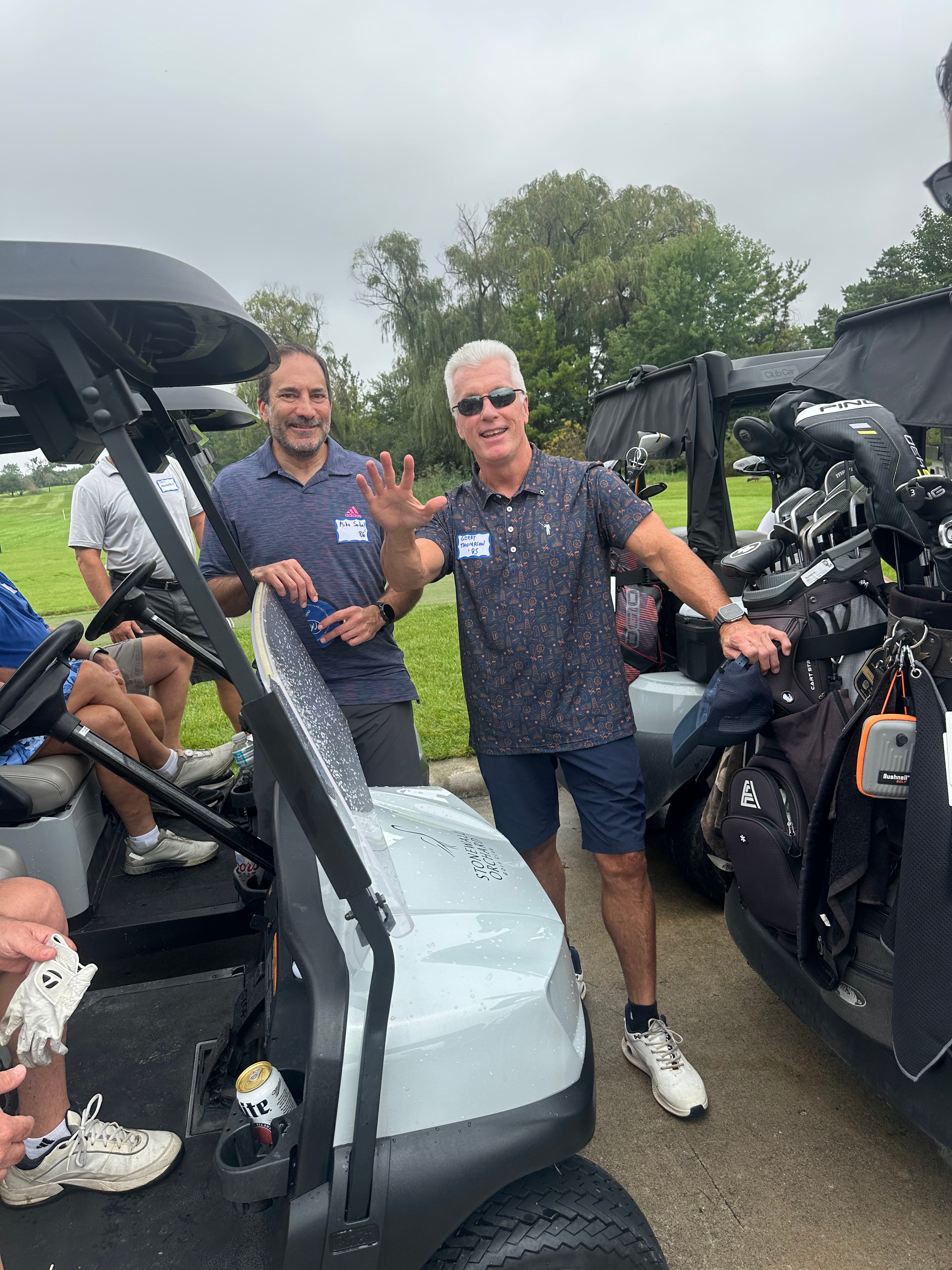 Two men posing with golf carts outdoors