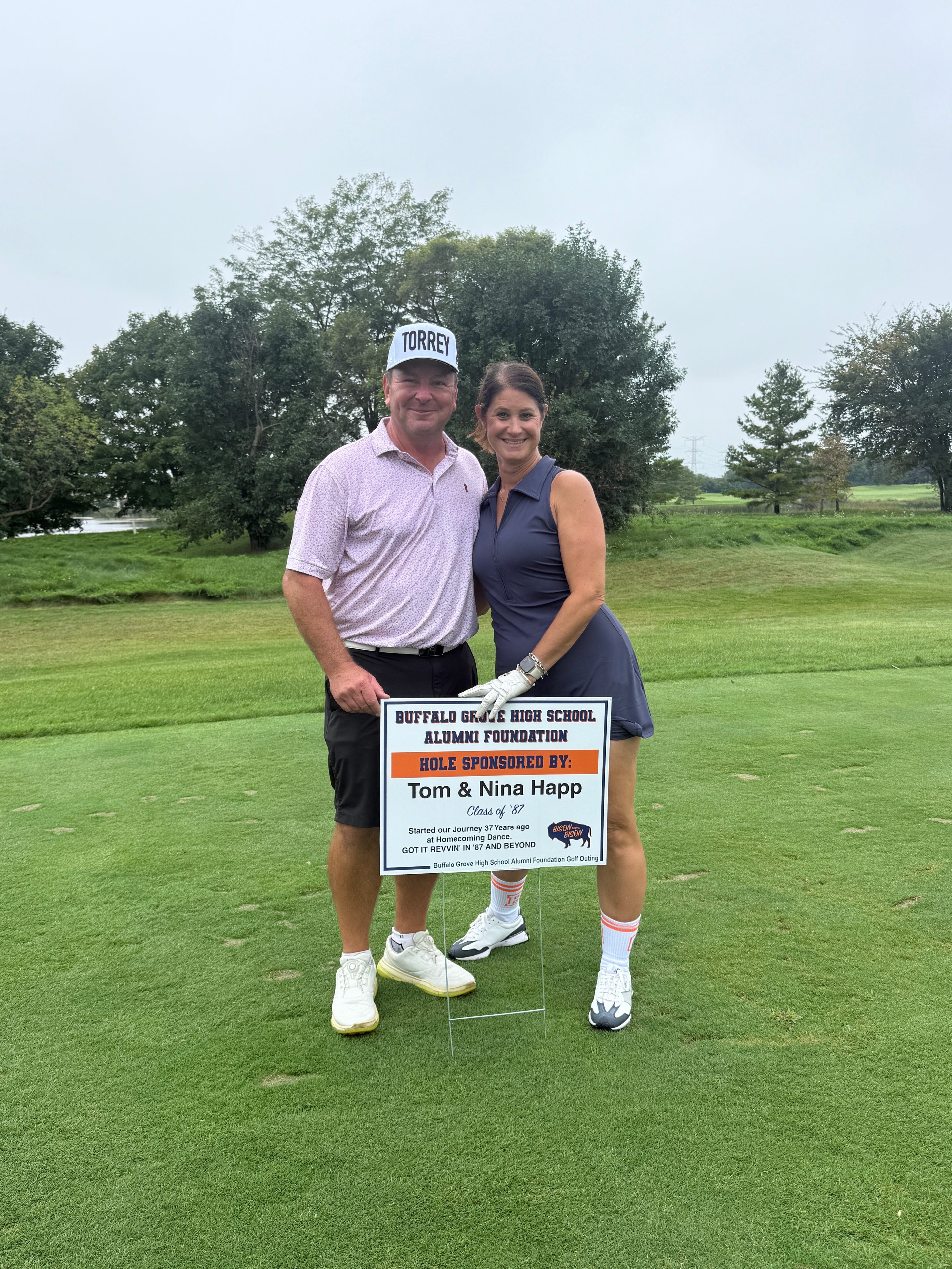 Couple posing by golf course hole sponsor sign