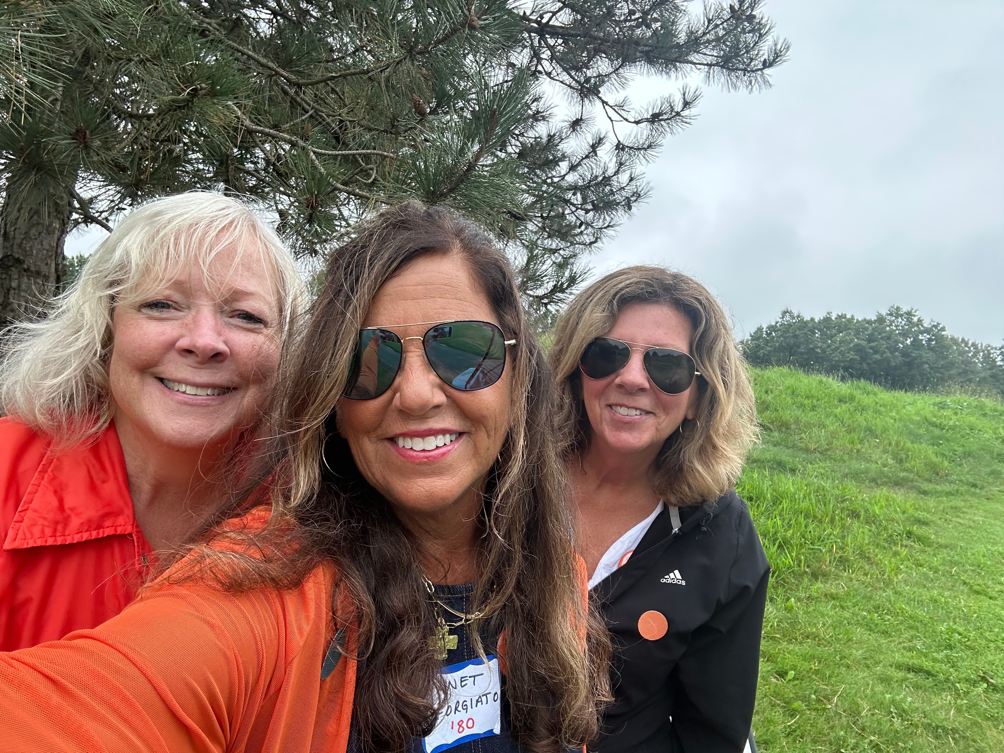 Three women smiling outdoors by pine trees