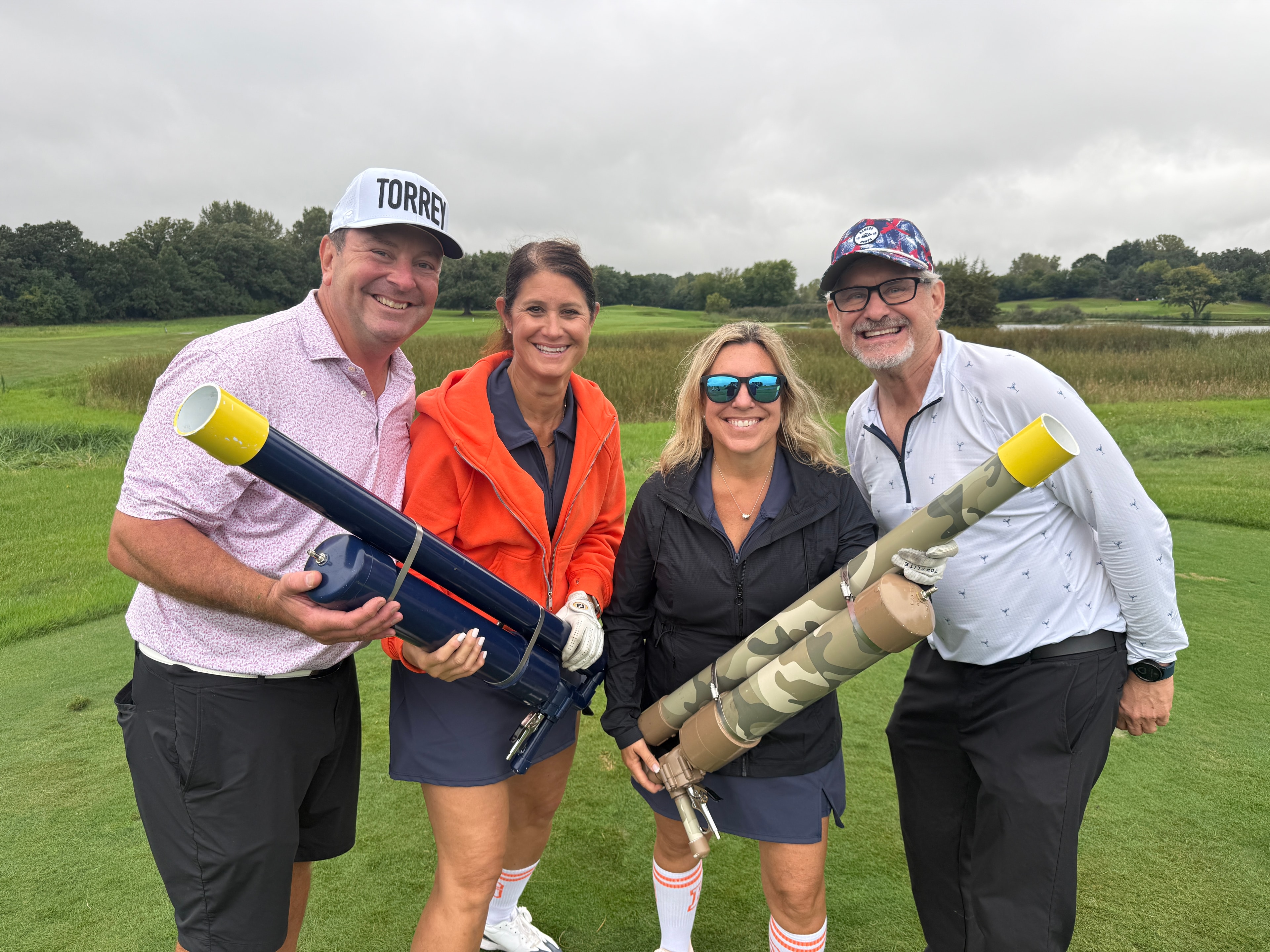 Four people holding golf ball cannons in field