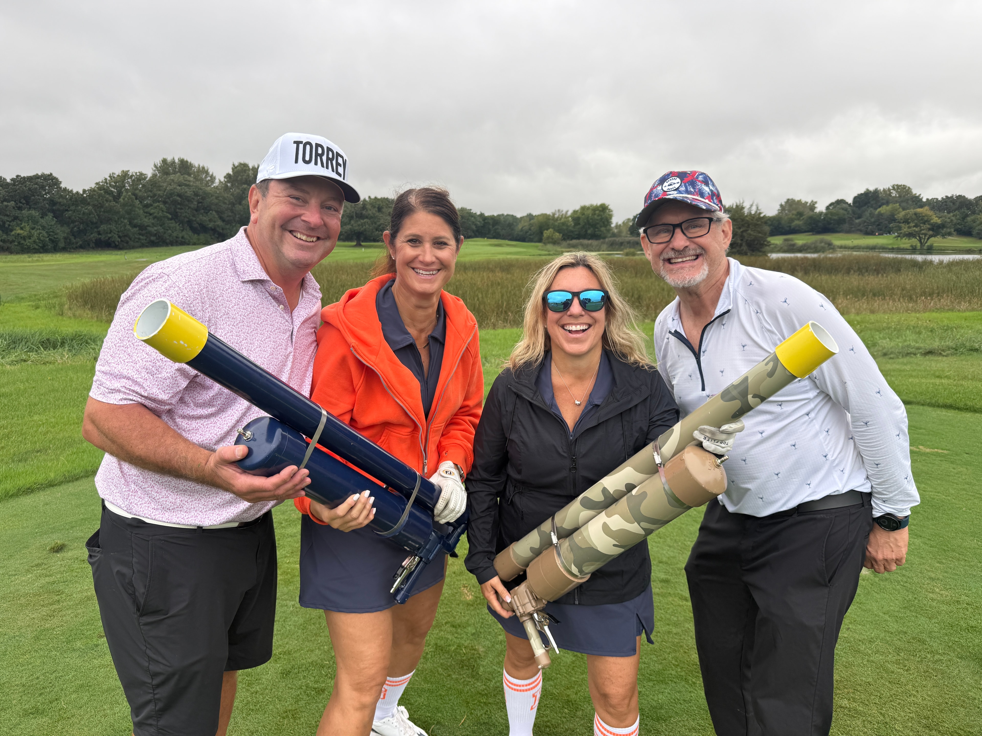 Four people holding golf ball cannons in field