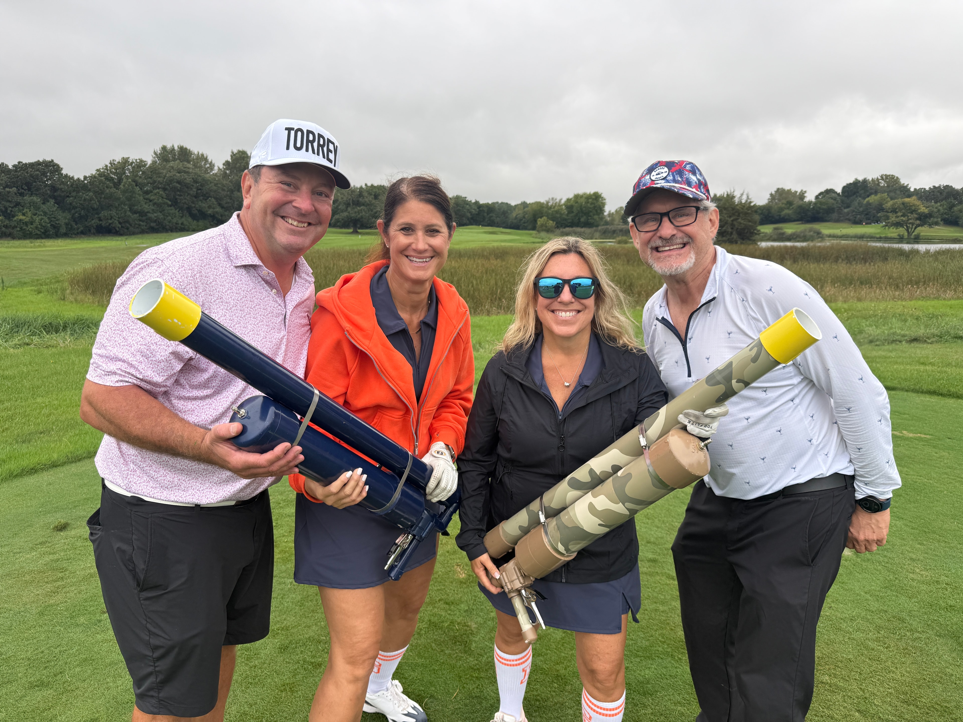 Four people holding golf cannons in field