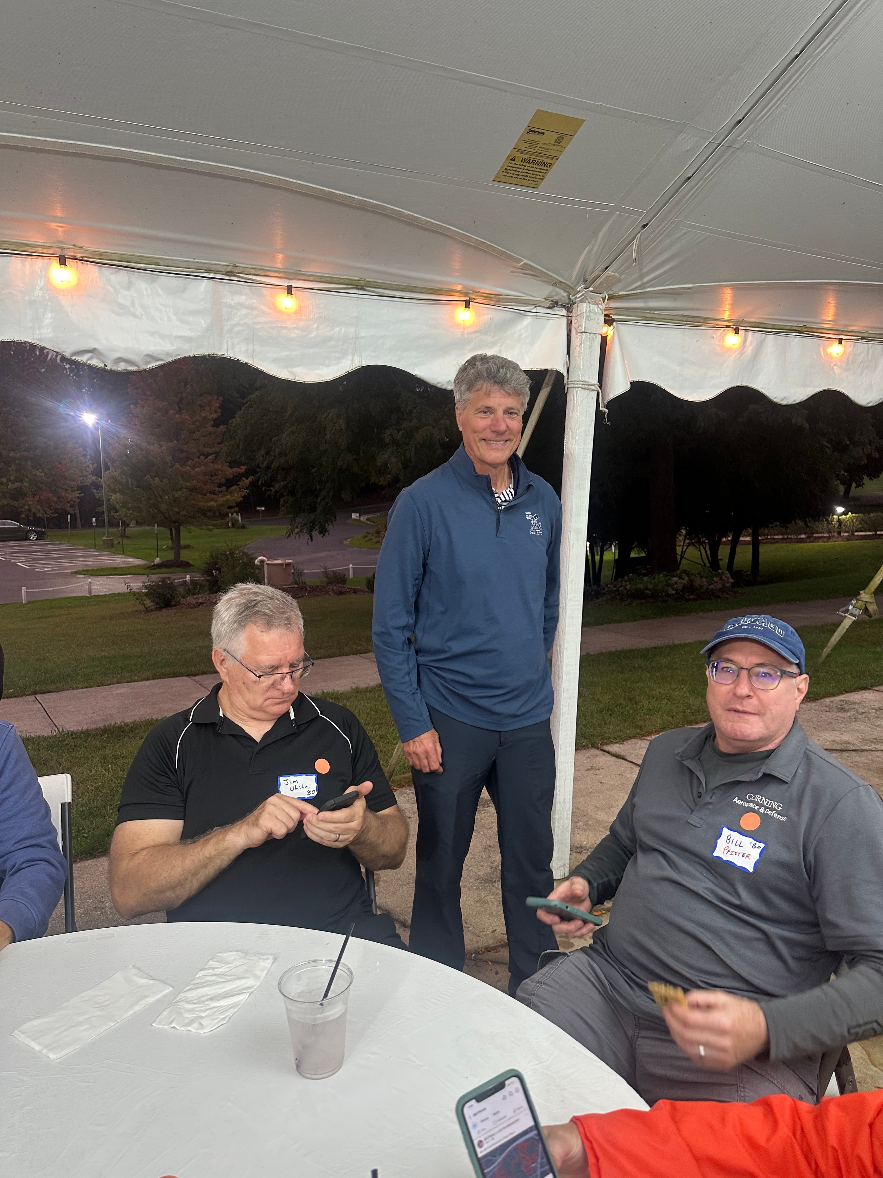 Three men gathered under outdoor tent evening