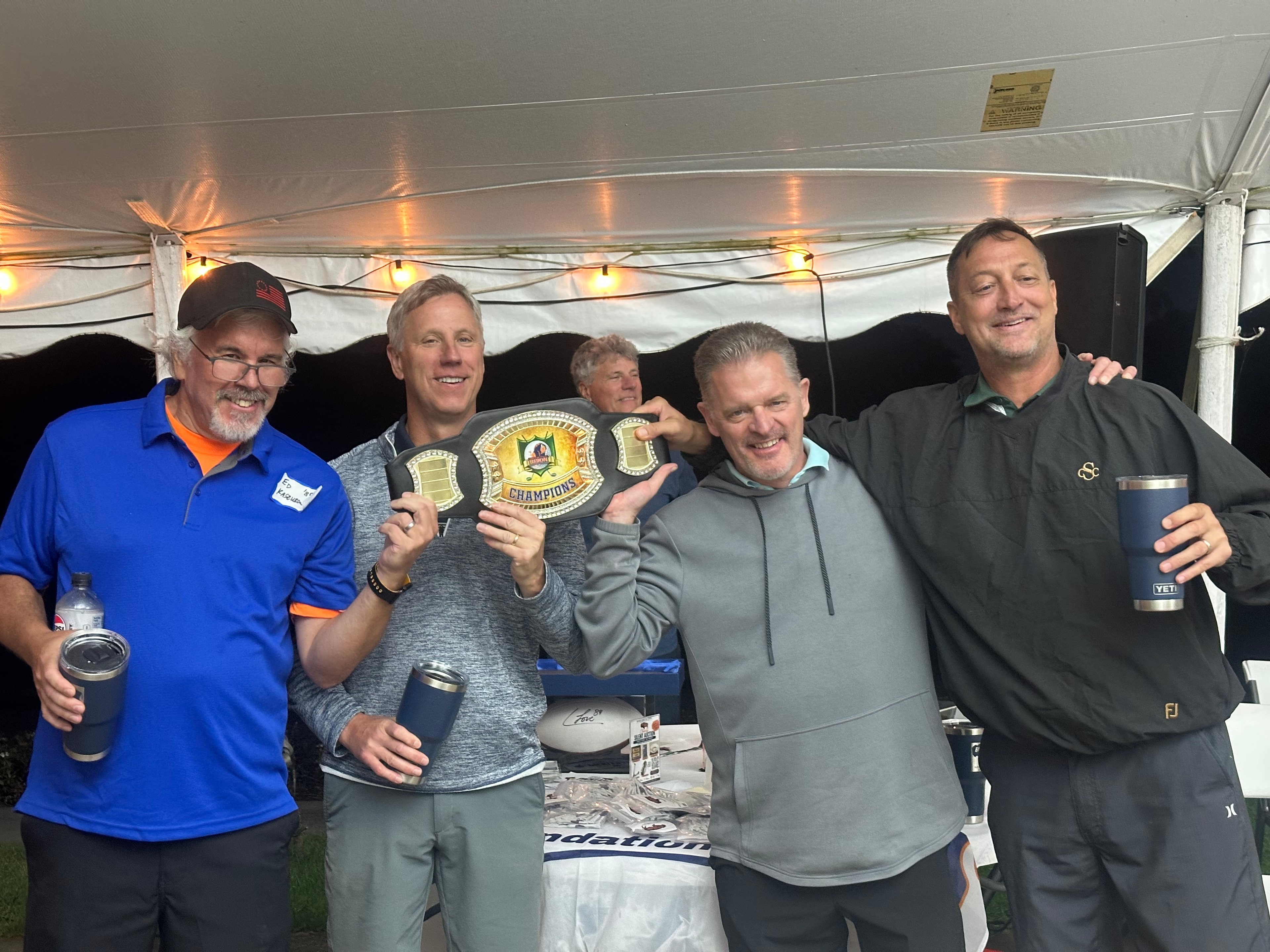 Men celebrating with championship belts under tent