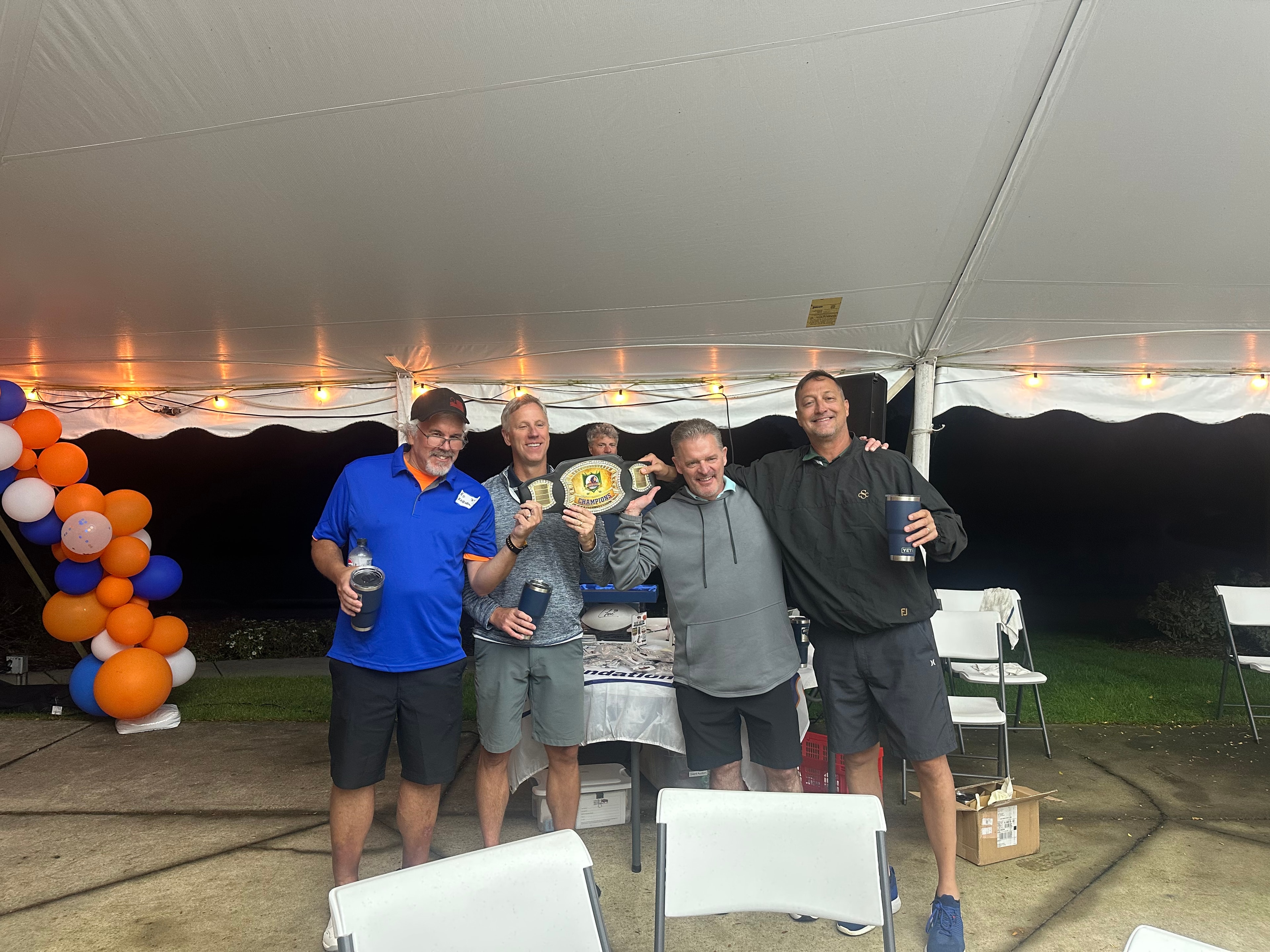 Men celebrating with championship belts under tent