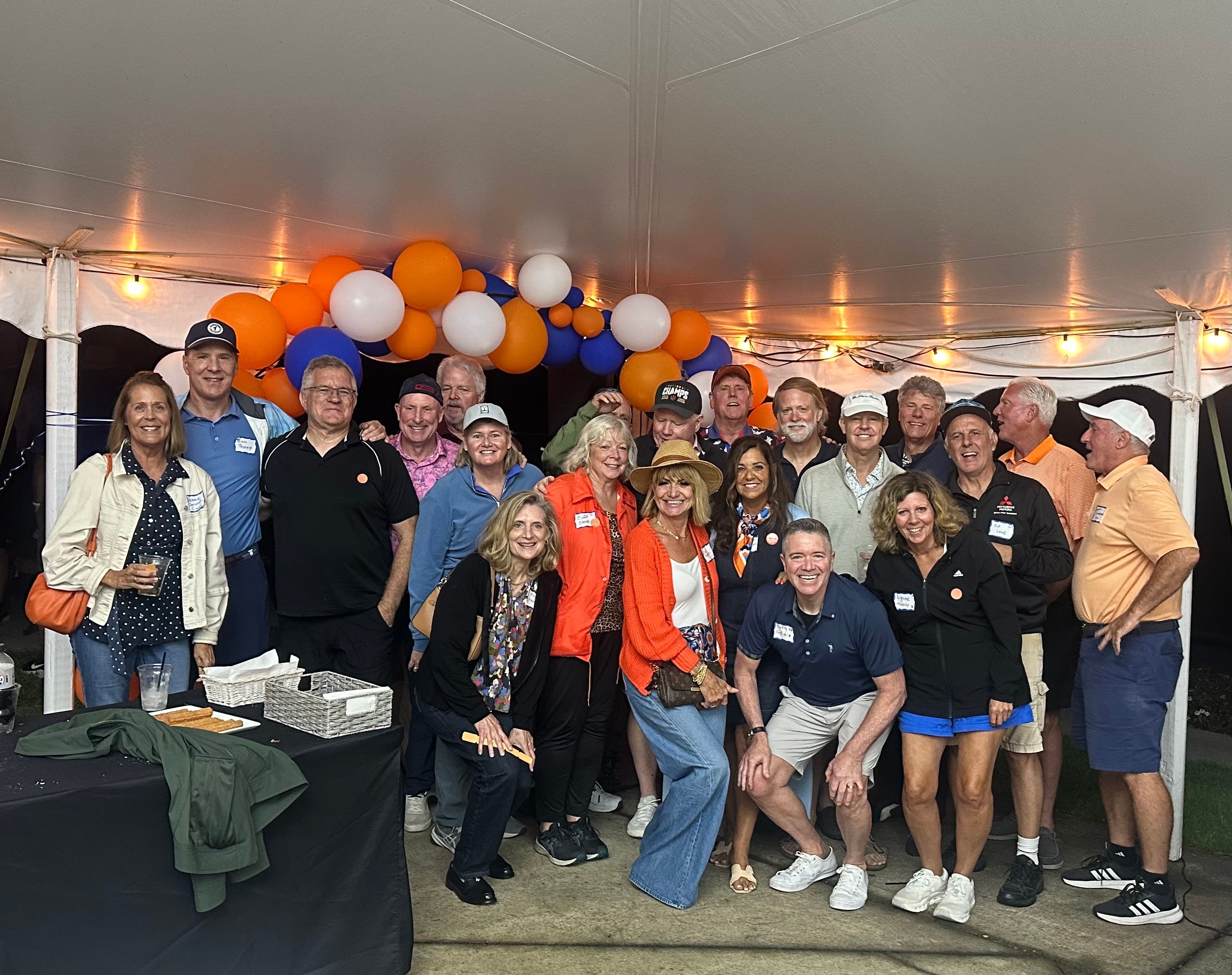 Large group posing under orange, blue, and white balloons