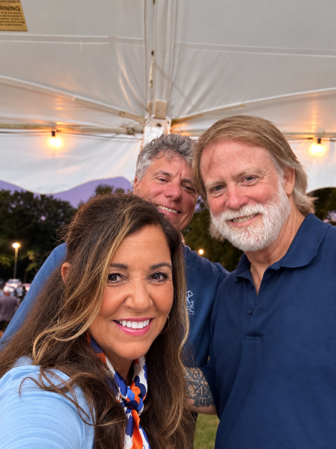 Three people smiling under tent evening